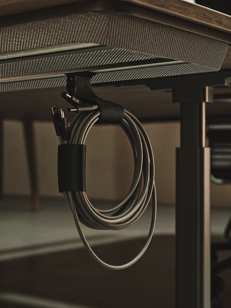 Gebündelte Kabel in Stoffschläuchen mit Klebeclips und kleiner Ablage unter der Tischkante